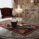 Tasse à café bronze et or Café des Délices présentée sur une table en marbre et nappe bordeaux