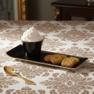 Tasse Café des Délices noir et or servie avec biscuits et chantilly, sur nappe à motifs dorés