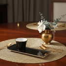 Tasse à café Café des Délices noir et or sur table en bois avec vase doré