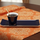 Tasse à café Café des Délices bleu marine et or sur nappe orange à motifs dorés